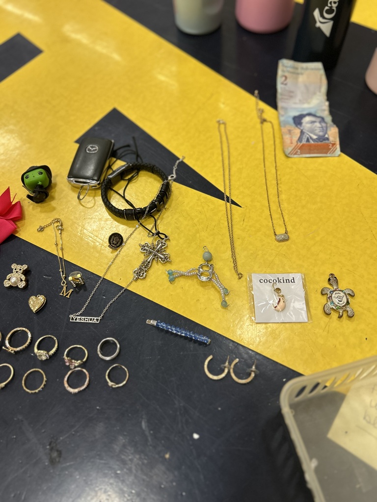 Various items on a yellow surface, including jewelry, a phone, a green toy, and a red flower.