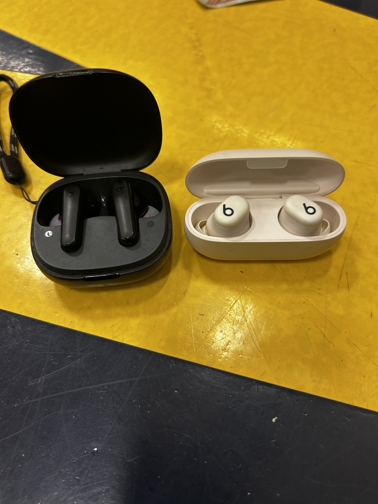 Two earbuds, one black and one white, in their respective open cases on a yellow surface.