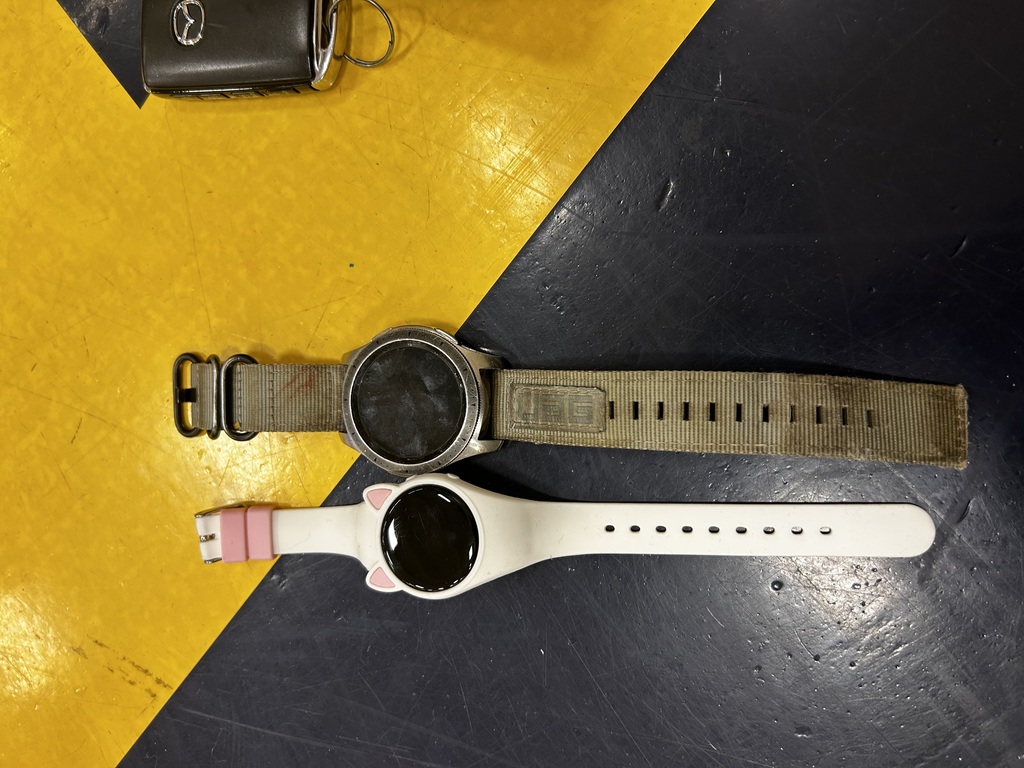 Two watches with different colored straps, one with a black dial and the other with a pink accent, sit on a black and yellow background.