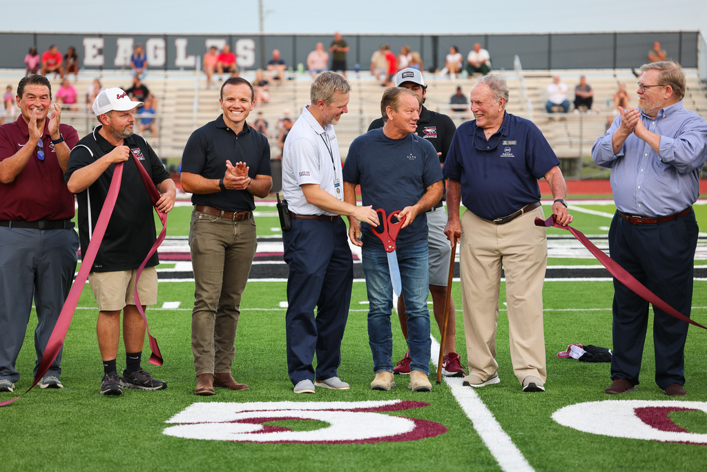 A group of people standing on a field holding ribbons. Some are cutting the ribbon with scissors.