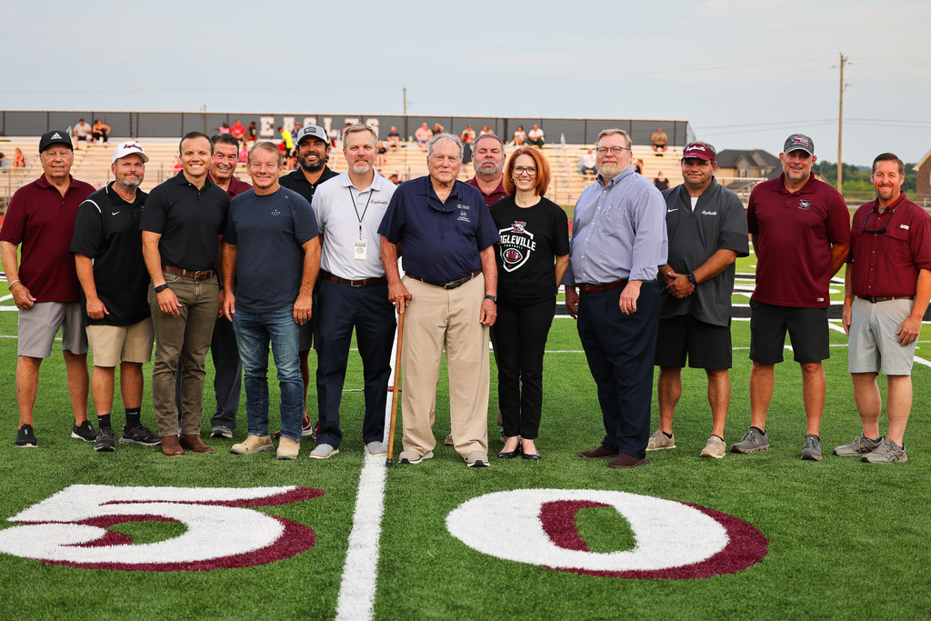 A group of people stand on a football field, wearing casual attire, with numbers 50 and 5 on the grass.