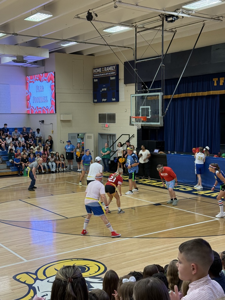 Basketball game indoors with players in blue and red jerseys. A crowd watches from the stands.