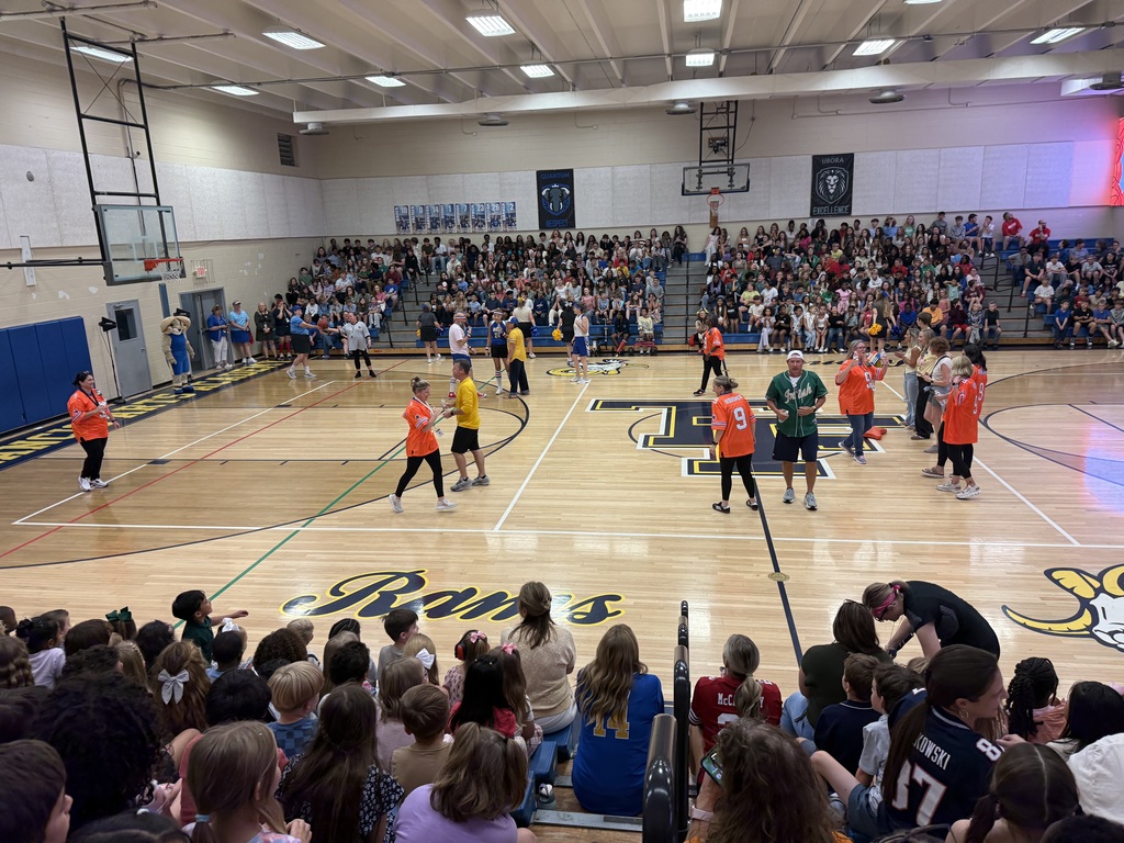 Multiple people playing a game of dodgeball on an indoor court. An audience of people watch from the bleachers.