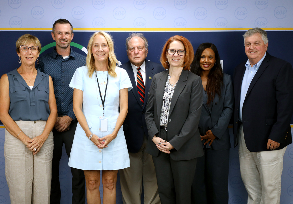 Group of adults posing in front of a blue wall with logos, including a green circle.