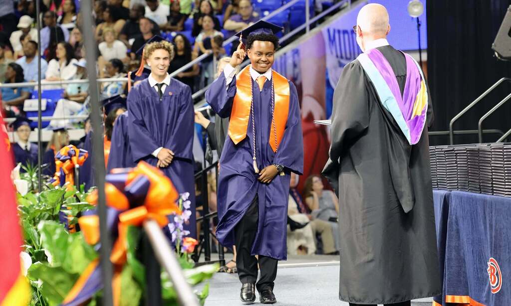 high school graduate in navy gown and orange stole accepts diploma
