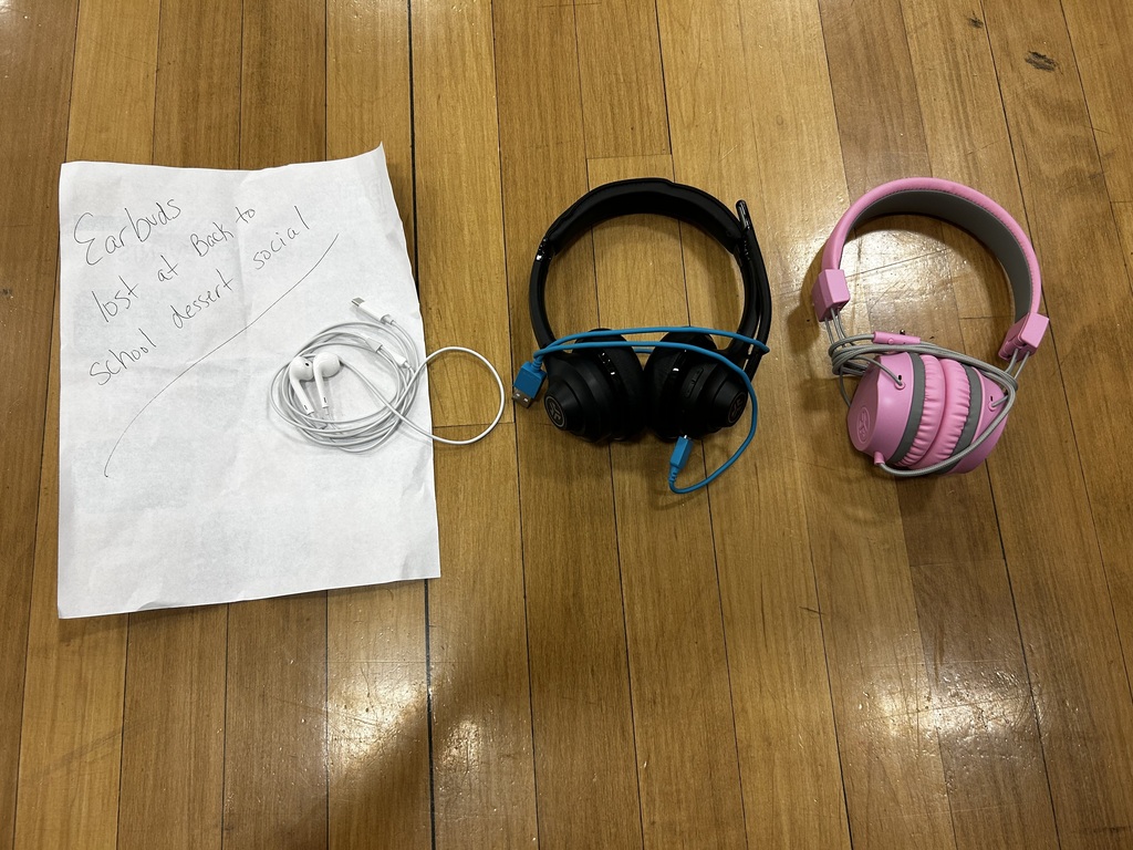 A white paper with writing, black and pink headphones, and a wire on a wooden floor.
