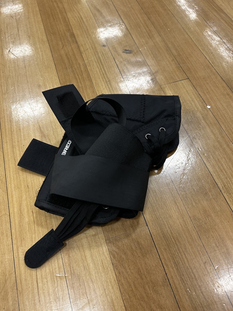 A black knee brace with adjustable straps and buckles is folded and placed on a wooden floor.