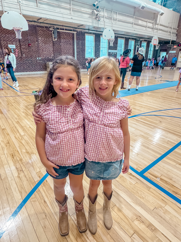 Two young girls in matching outfits and cowboy boots pose together on a basketball court.
