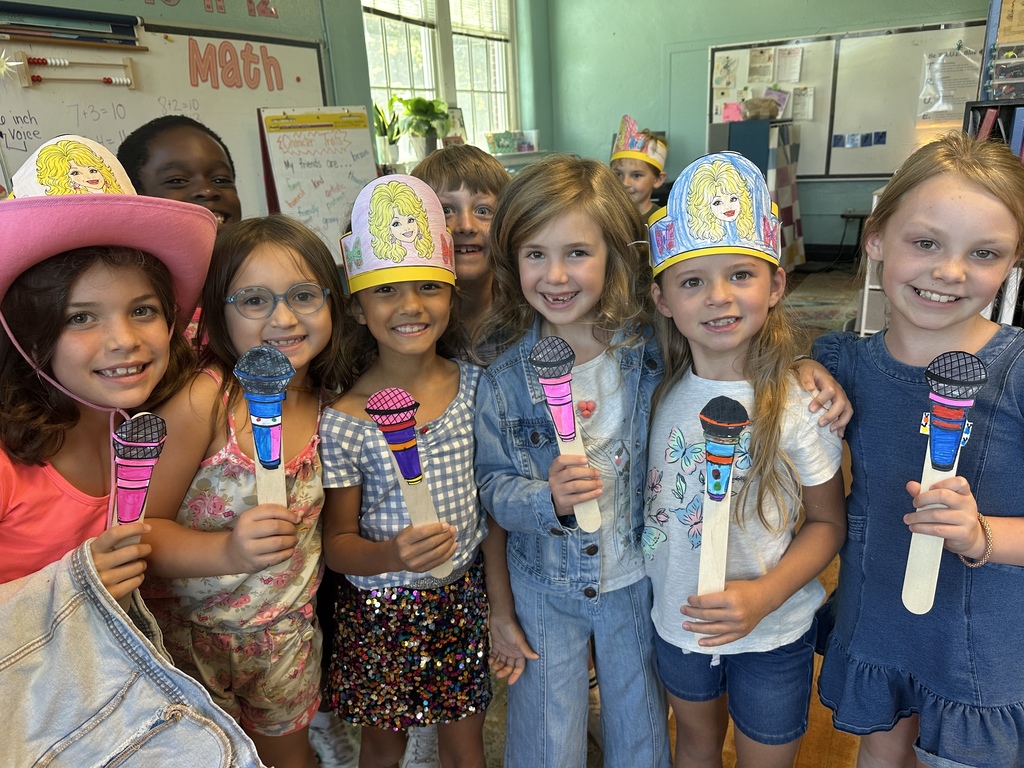 A group of children in a room wearing themed hats and holding craft items for a photo.