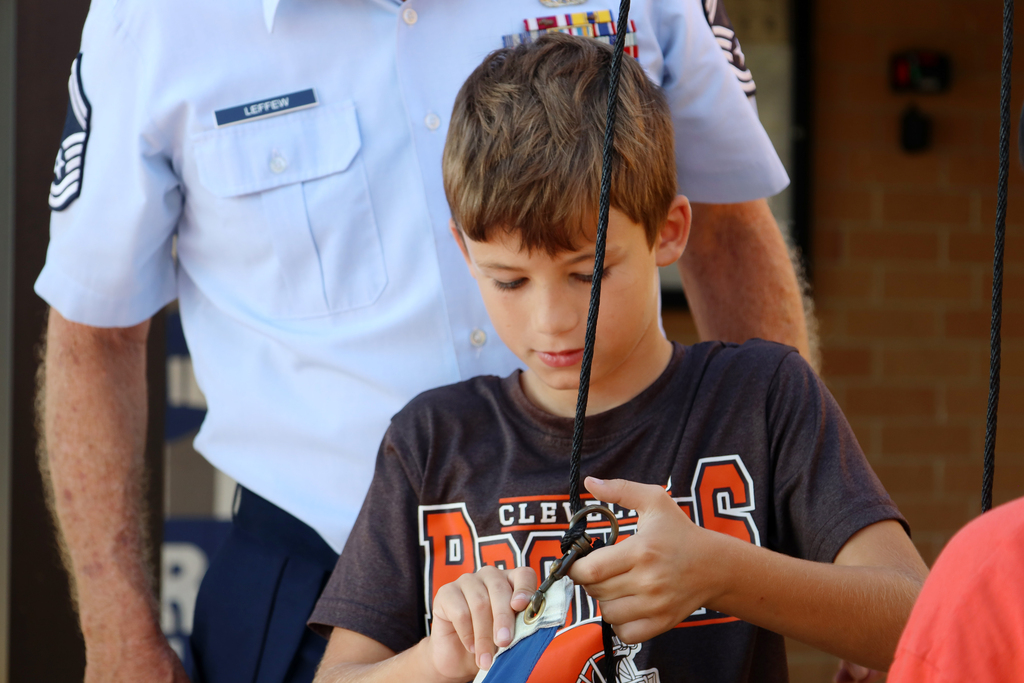 A boy wearing a t-shirt with a graphic on it examines a ball, while an adult in uniform stands behind him.
