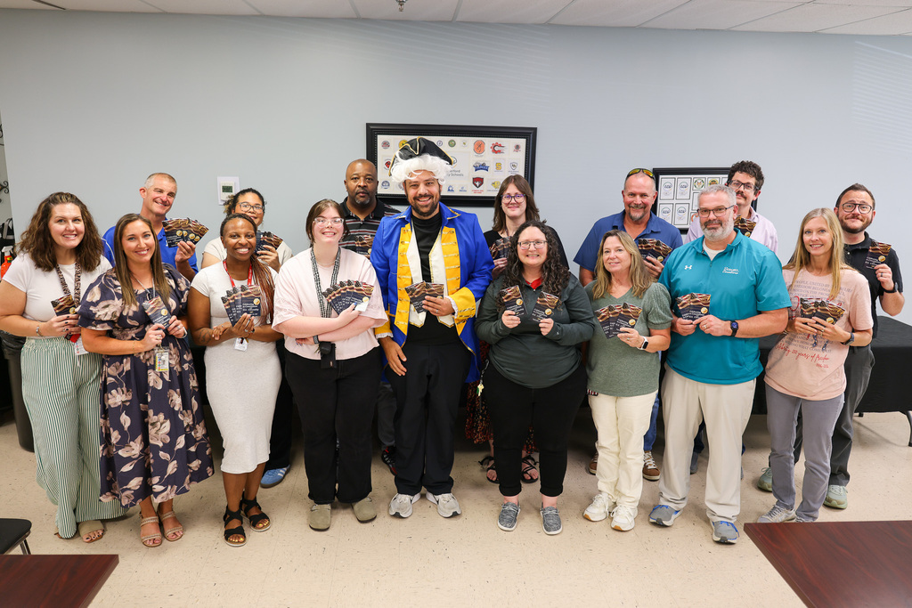 A group of people stands together in a room, posing for a photo. They hold certificates.