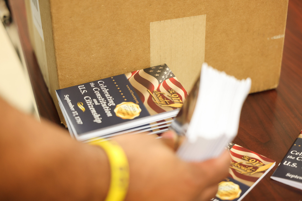 Person cutting through stack of booklets with American flag designs. A box is behind the booklets.