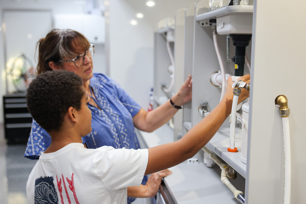 An adult and a child working on a machine. The adult wears glasses and a blue shirt. The child wears a white shirt.