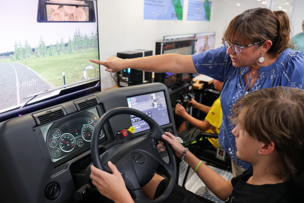 Woman and child in a training simulator; woman points to screen, child holds steering wheel.