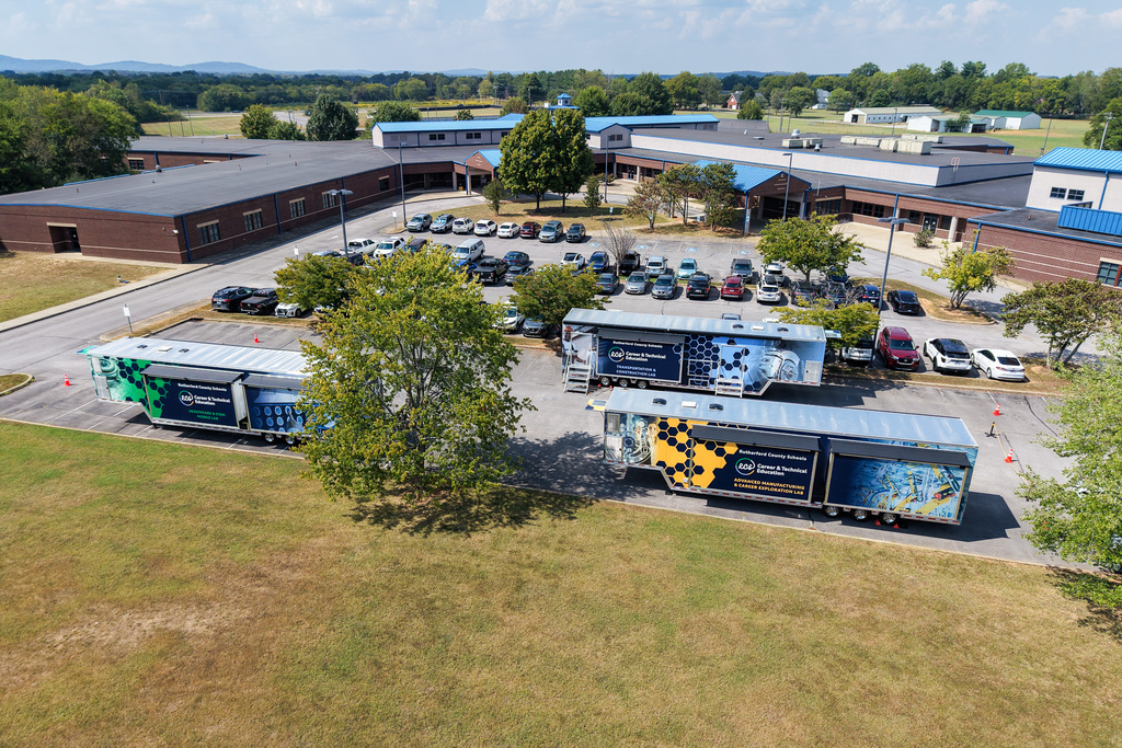 Aerial view of school buildings with cars parked in the lot and two trucks in the front.