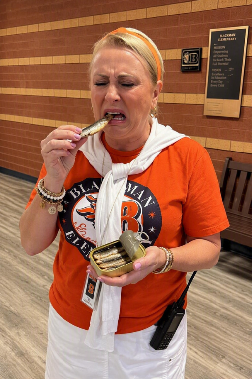 An adult female in an orange shirt and white scarf eats a small fish from a metal tin.