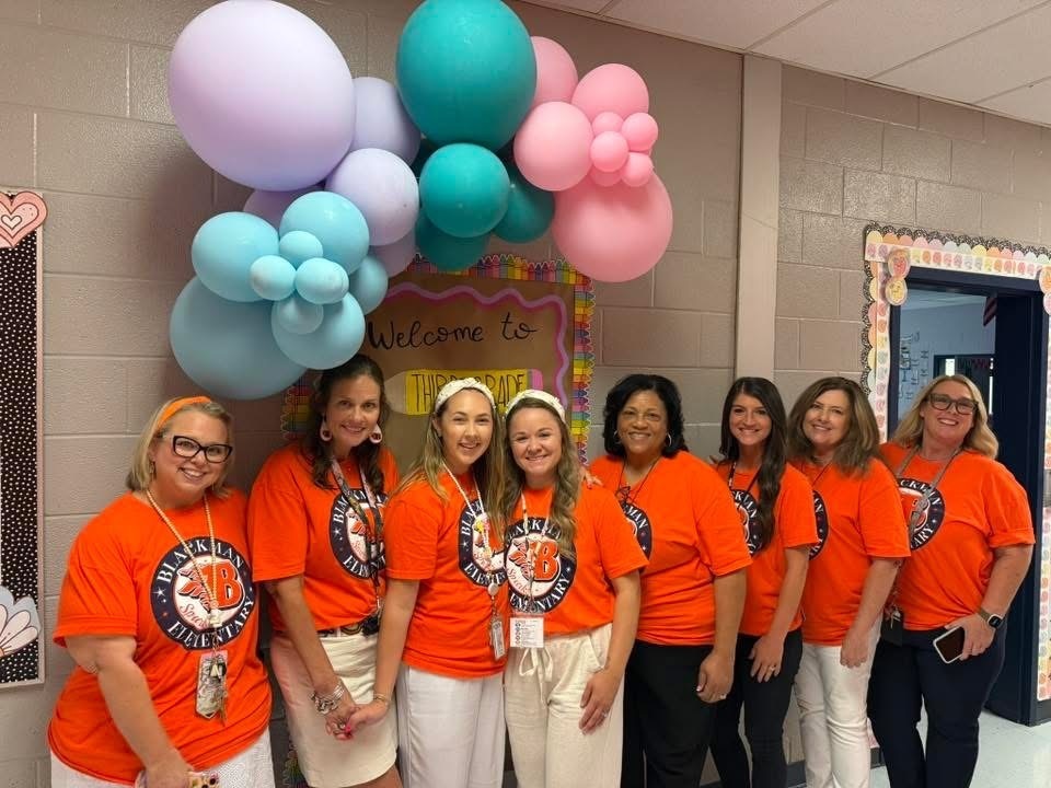A group of women in orange T-shirts and white pants pose for a photo in a room.