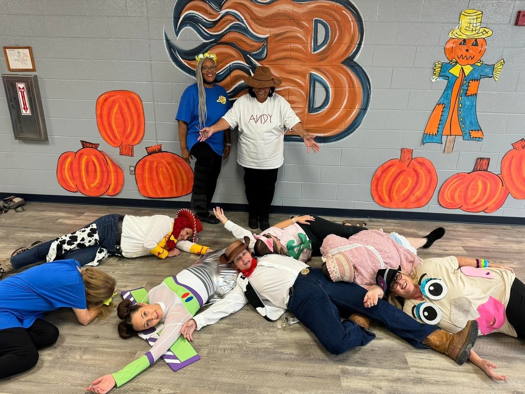 Group of people lying down on a floor. Two people standing with a pumpkin mural behind them.