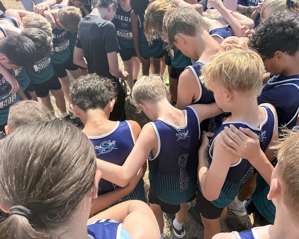 A group of individuals in sports attire stand in a circle, facing each other, with hands on shoulders.