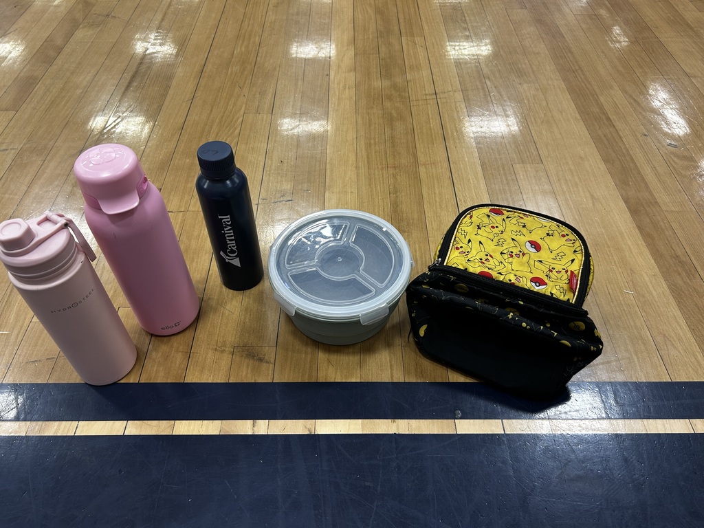 A wooden floor displays four items: a pink thermos, a black bottle, a container with a lid, and a small bag.