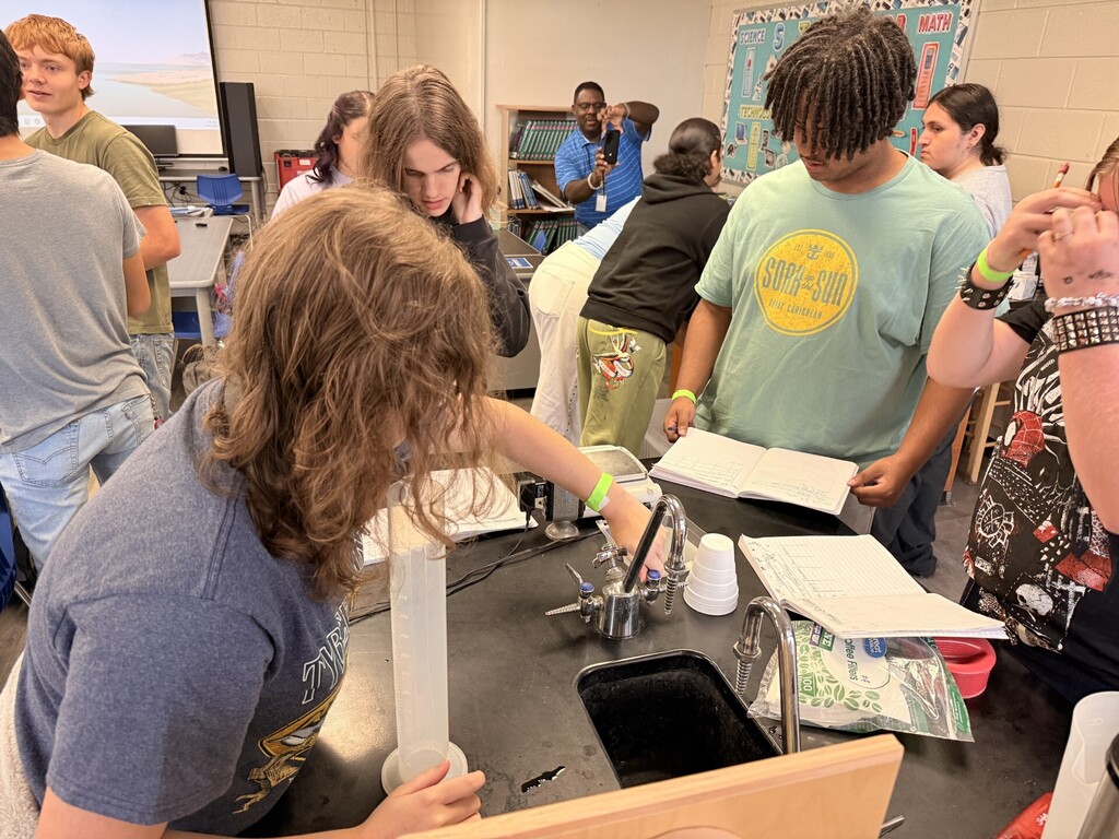 Group of students in a classroom lab. One student pours liquid from a beaker into a funnel.