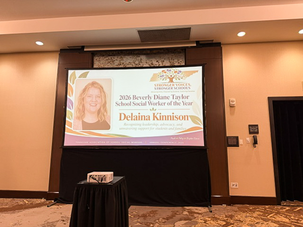 Screen announcing Delaina Kinnison as social worker of the year with a picutre of her smiling on it