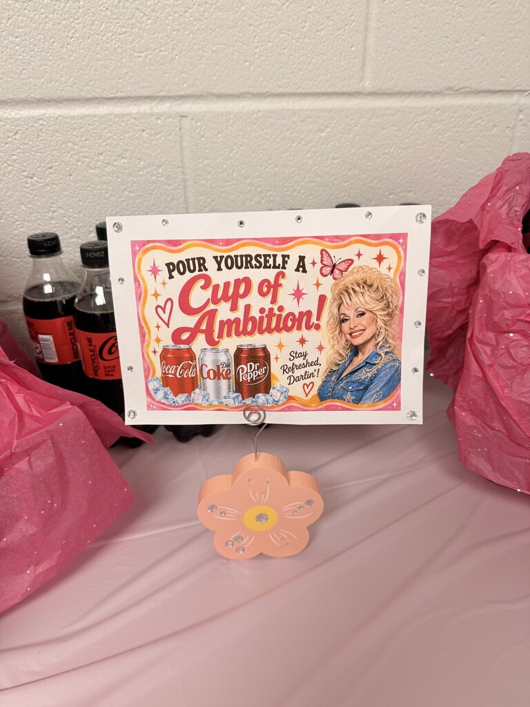 Sign says "Pour yourself a cup of ambition" with a picture of Dolly Parton. Bottles of Coke are behind the sign.