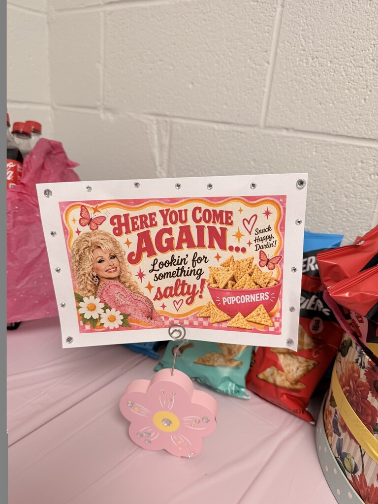 A sign with a picture of a blonde woman saying "Here You Come Again... looking for something salty!" sits on a pink surface.