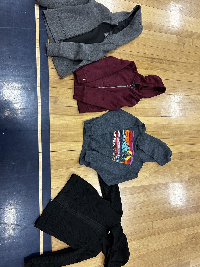 Four sweatshirts of various colors and patterns, along with a pair of black pants, are neatly laid out on a wooden floor.