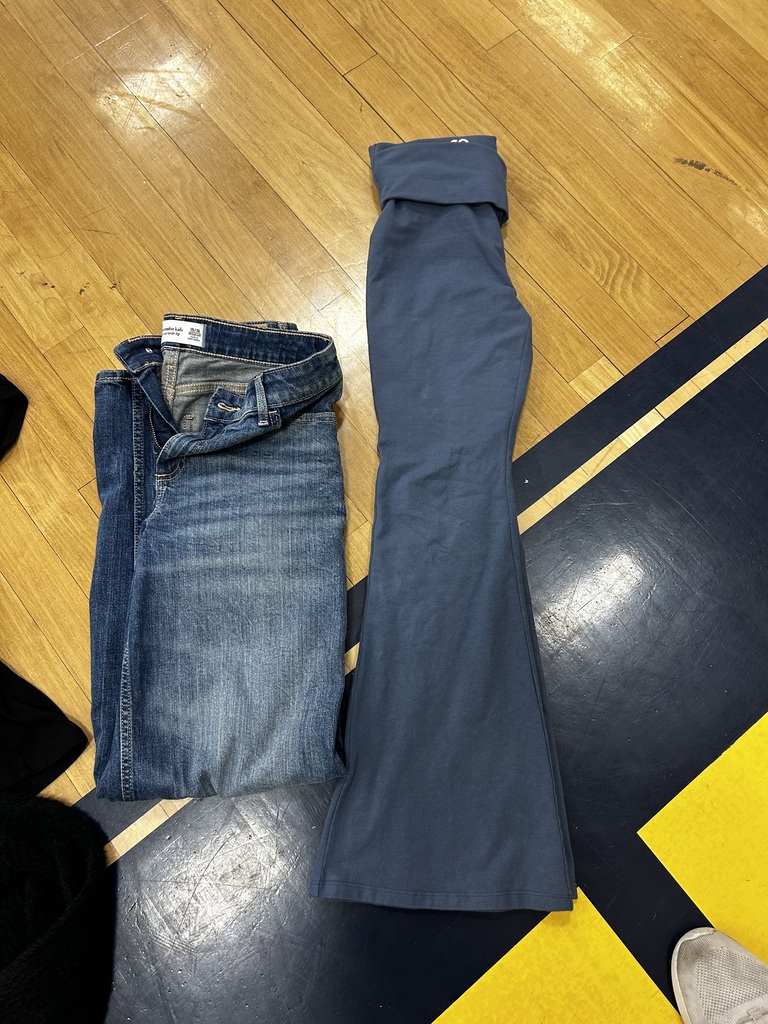 A pair of blue jeans and a pair of blue flared pants lie on a wooden floor.