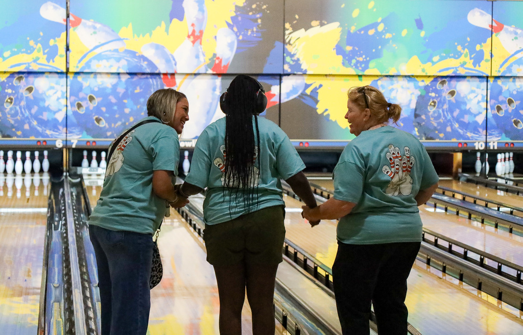 Two staff members and a student facing the bowling lane, holding hands.