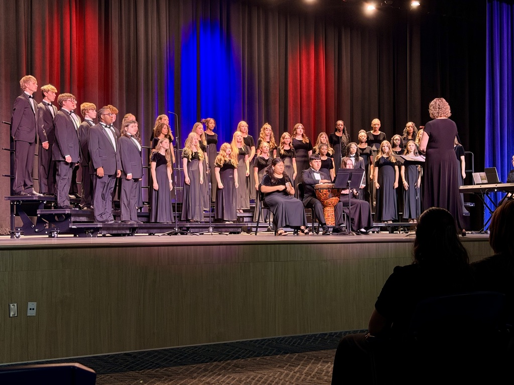 A choir performs on a stage with a red and blue backdrop, with some members seated.