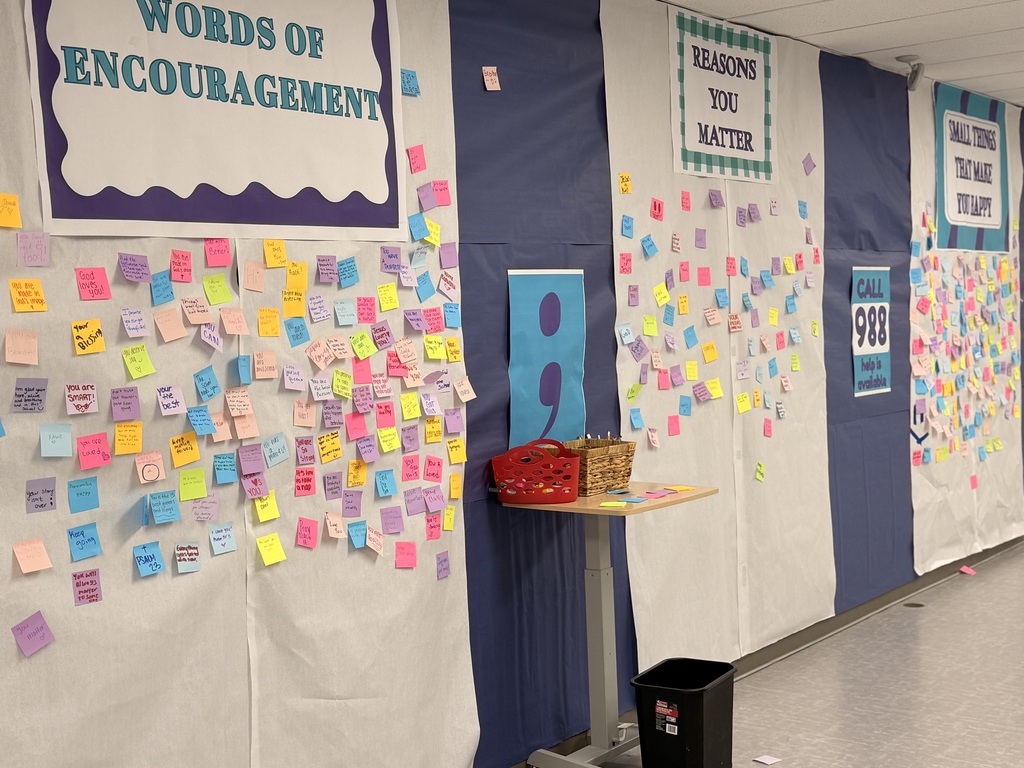 A wall with colorful sticky notes and a table. Words of encouragement are on the wall.