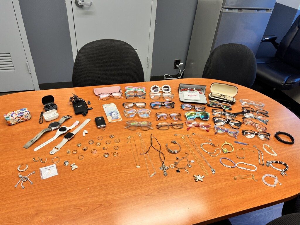 A desk displays various items including watches, sunglasses, bracelets, and other accessories on a wooden surface.