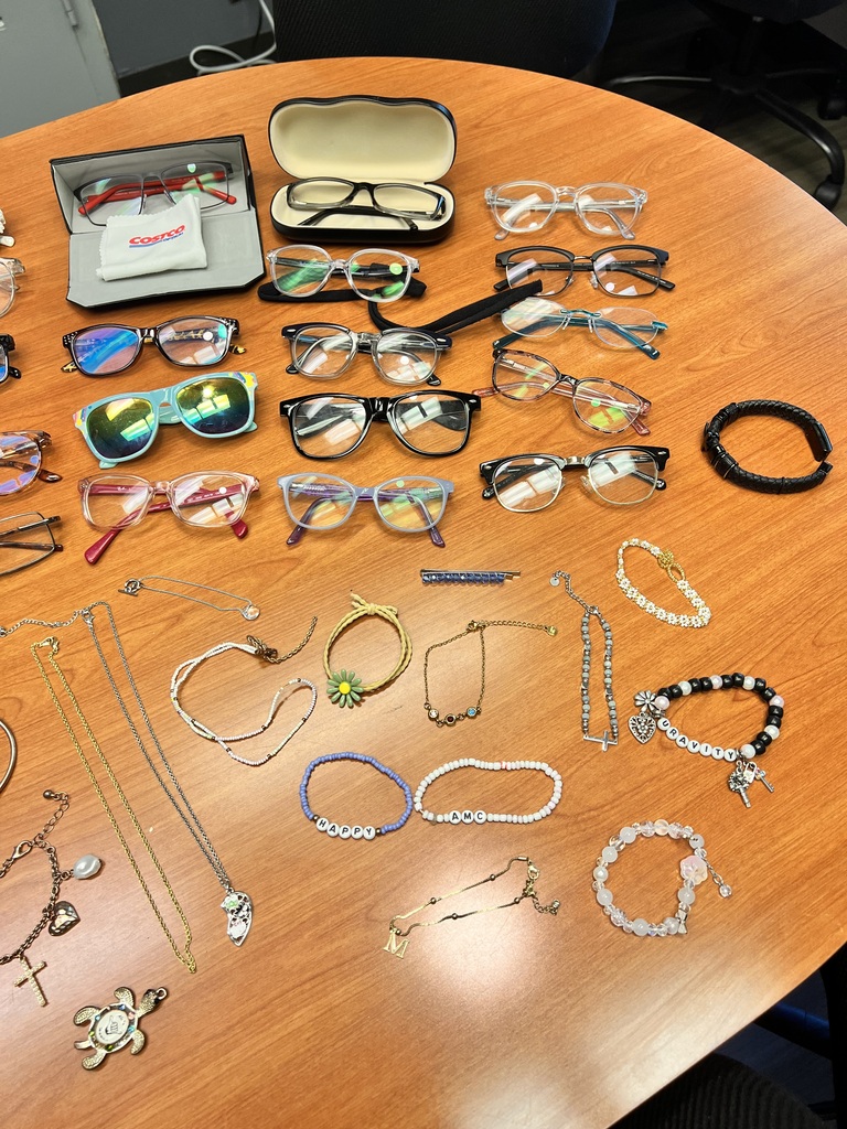 A wooden table displays various items, including glasses, sunglasses, necklaces, and bracelets, all neatly arranged.