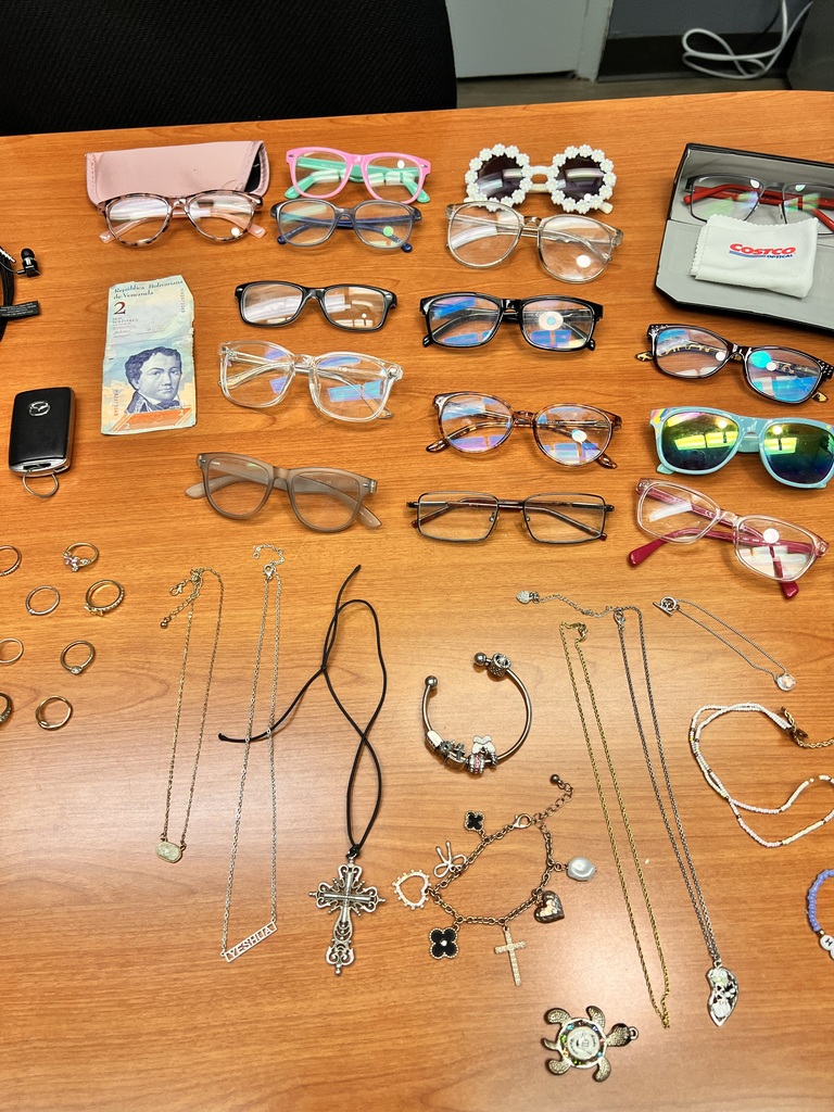 A table displays sunglasses, jewelry, a phone, and a wallet. The items include necklaces, bracelets, rings, and various glasses.