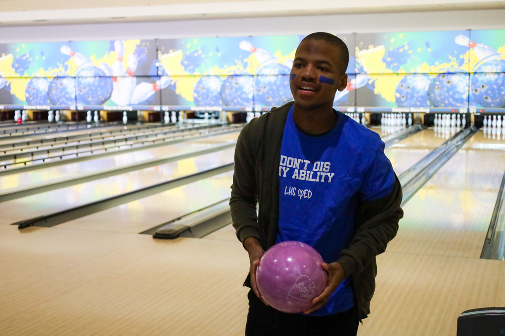 Student holding a bowling ball with bowling lanes behind him