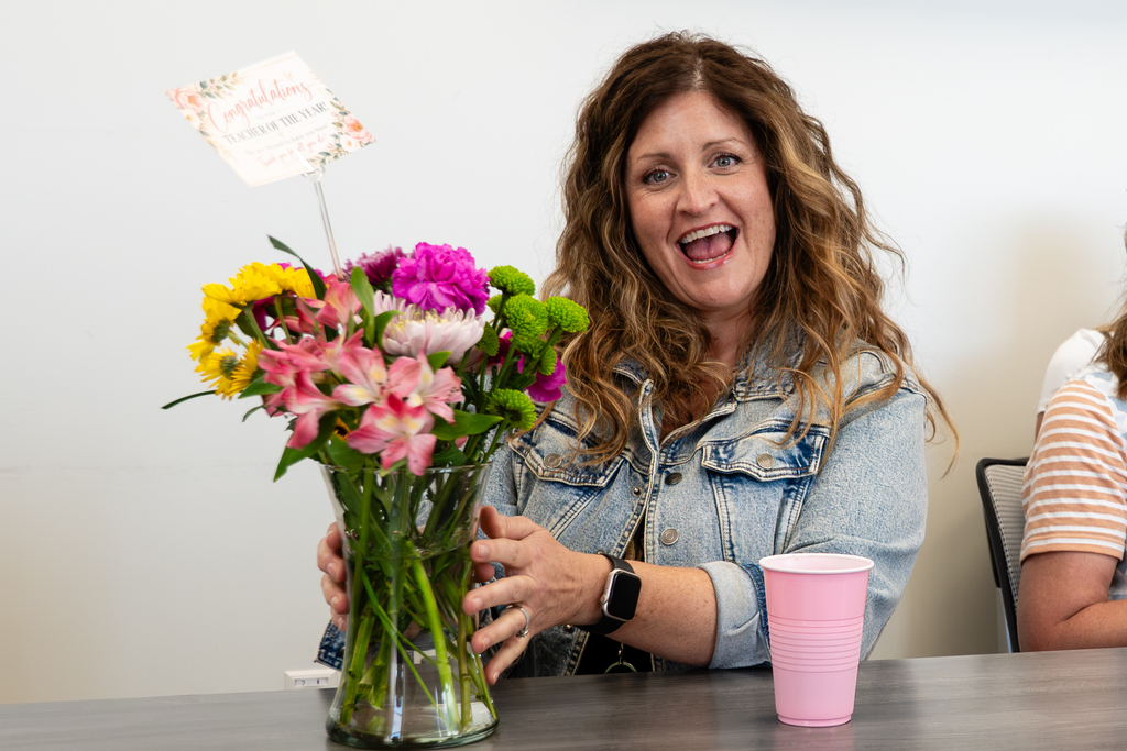 Woman holding a vase of flowers, seated at a table, with a pink cup in front.