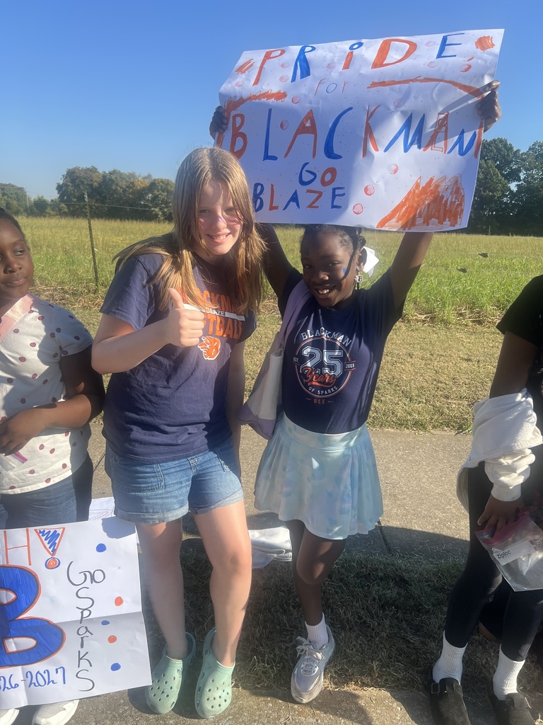 Four young individuals hold up signs in front of a grassy field. One holds a sign with the words "Pride Blackman Go Blaze."