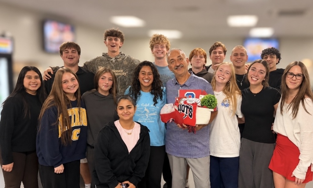 A group of students standing together, some holding gifts, in a brightly lit indoor area.