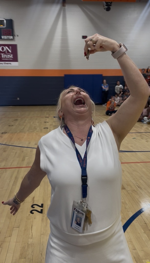 A woman with an ID badge is cheering and holding a small object in a gymnasium.