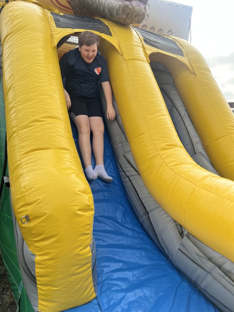 A person in a black shirt and shorts slides down a yellow and gray inflatable slide.