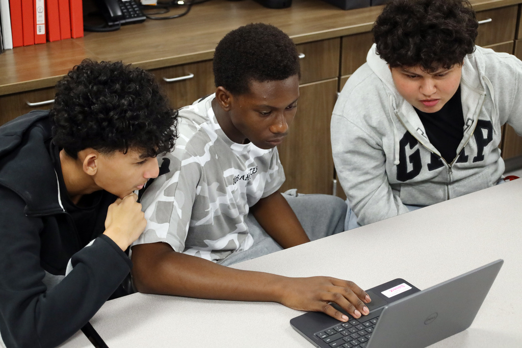 Male students huddle around laptop to review classwork