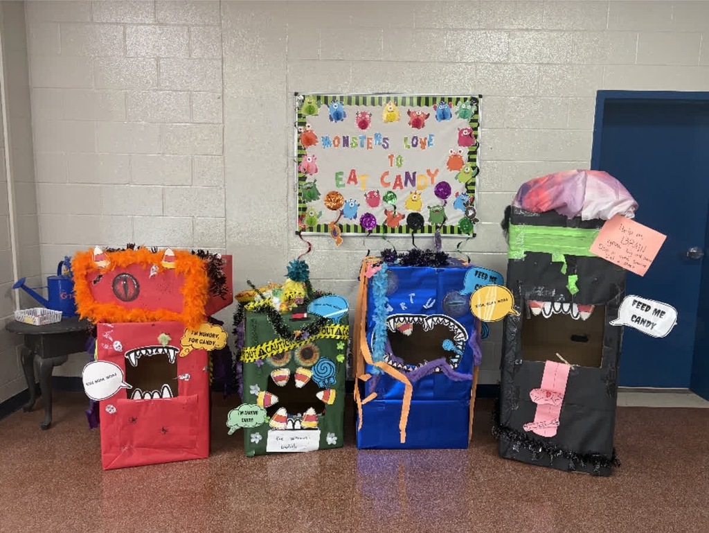 Several boxes decorated as monsters line up against a wall. A bulletin board is above the boxes.