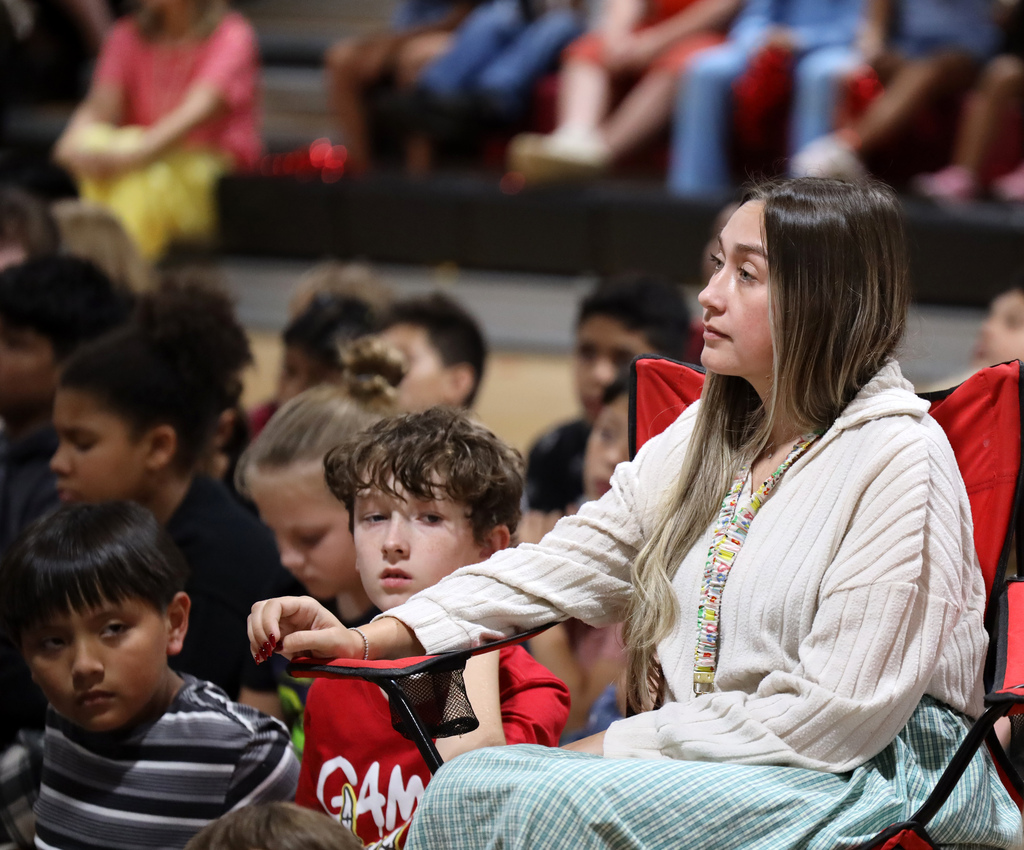 Woman in a white sweater and blue skirt sitting on a red chair holds a tablet.