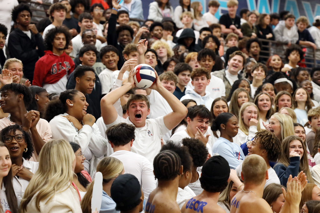 A group of students cheering in stands; one student holds a ball above their head.