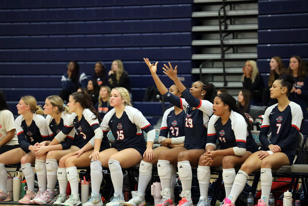 Group of female athletes in blue and white jerseys seated on a bench in a sports facility.