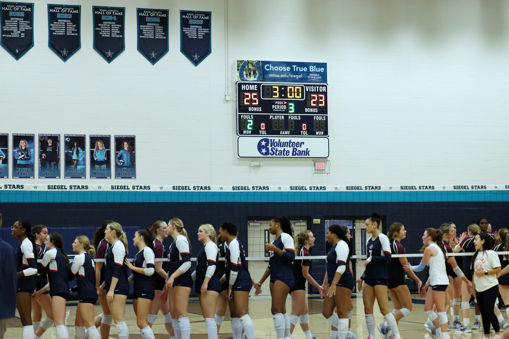 A team in blue and white uniforms walks along a court. A scoreboard shows two scores.