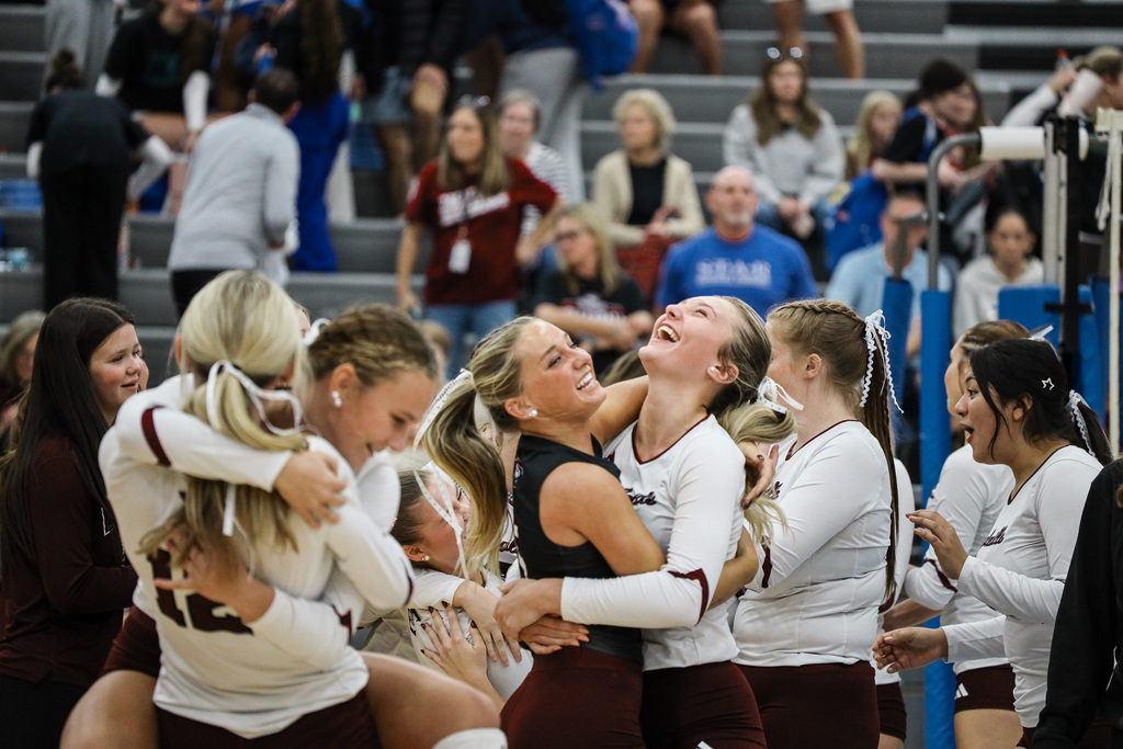 Group of women celebrating on a court, one woman looks up, and others hug her.