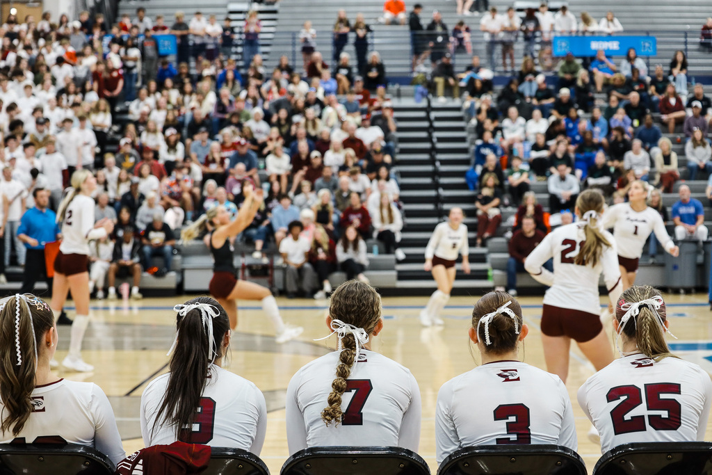 Four seated players with ponytails and numbered jerseys; a player jumps to spike the ball.